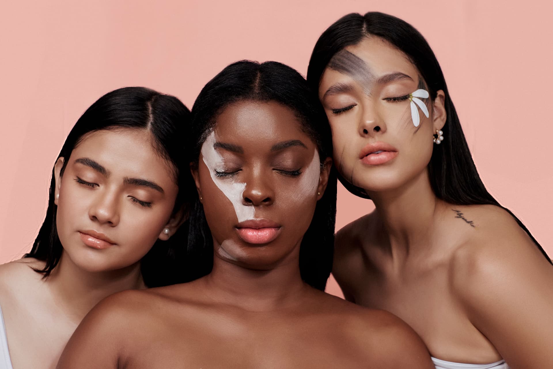 Three women with skincare on their faces against a soft blush backdrop